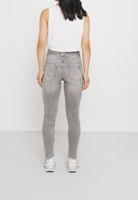 Pantalones vaqueros de talle alto grises con un corte ajustado, que cuentan con bolsillos traseros y una tela texturizada. Combinados con zapatillas blancas para un look casual.