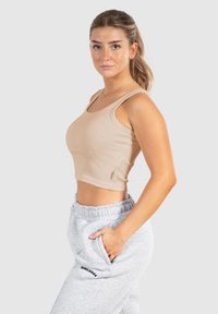 Top corto beige a costine con spalline large, abbinato a pantaloni della tuta grigio chiaro con logo. Il design è aderente, enfatizzando la vita.