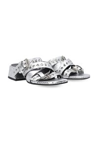 Zilveren sandalen met brede straps, metallic afwerking, studs en een lage blokhak. Getextureerd oppervlak met een mix van glanzende en matte gebieden.