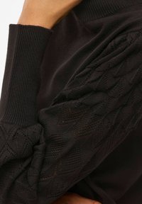Pull noir avec des poignets côtelés et un design texturé à motifs sur les manches. Le tissu semble doux avec une finition légèrement brillante.
