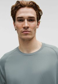 Lysegrå, tekstureret atletisk skjorte med rund halsudskæring og raglanærmer, med subtile syningsdetaljer.