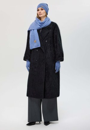 Cappotto doppiopetto nero e peloso, abbinato a una sciarpa e a un cappello blu. I pantaloni grigi a gamba larga e i guanti blu completano l'outfit, con tacchi a spillo neri.