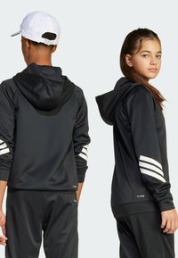 Felpa nera sportiva con cappuccio, dettagli a tre strisce bianche sulle maniche e una texture liscia. Adatta per sport o abbigliamento casual.