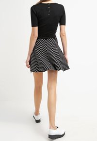 Zwarte top met korte mouwen en knoopdetail aan de achterkant, gecombineerd met een zwart-witte zigzagpatroonrok. Witte plateau-schoenen.