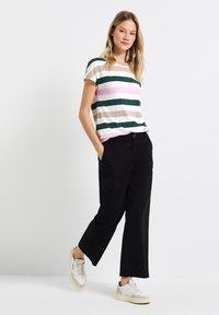 T-shirt a righe con maniche corte, caratterizzato da strisce verdi, rosa e beige. Abbinato a pantaloni larghi neri e sneakers bianche.
