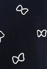 Marinblått tyg med vita broderade bågar, där varje båge pryds av en liten silverdetalj, vilket skapar ett strukturerat mönster.