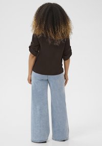 Chemise noire à boutons avec des manches retroussées, associée à un jean en denim large de couleur bleu clair. Des boucles texturées visibles à l'arrière.