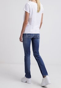 Camiseta blanca de manga corta combinada con jeans de mezclilla azules, con un corte slim, ligeras decoloraciones y zapatillas blancas de plataforma.