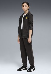 Felpa nera con zip e logo, t-shirt bianca, pantaloni neri abbinati e sneakers nere. Tessuto morbido, vestibilità rilassata e polsini a costine.