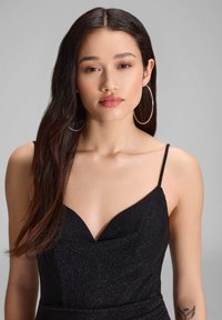 Musta, hihaton mekko V-pääntiöllä kiiltävässä, teksturoidussa kankaassa. Sisältää ohuita olkaimia ja istuvan siluetin.