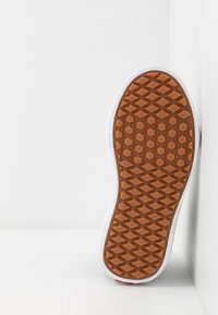 Bruine rubberen schoenzool met een diamantpatroon, witte zijkanten en een rode accent bij de hak, geplaatst tegen een witte achtergrond.