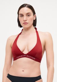 Rød halter bikini topp med dyp V-hals. Har en merket stropp med "TOMMY HILFIGER" tekst og en jevn, elastisk stoffoverflate.