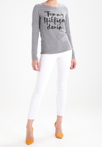 Harmaa pitkähihainen paita, jossa on musta "Tommy Hilfiger denim" -teksti, yhdistetty valkoisiin skinny-farkkuihin ja keltaisiin korkokenkiin.