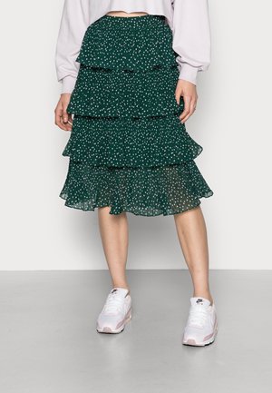 Grüner Stufenrock mit weißen Punkten, aus leichtem Stoff. Kombiniert mit weißen und pinken Sneakers.