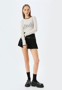 Transparante witte kant lange mouwen top met zwarte rand, gecombineerd met een zwarte geplooide miniskirt met een gesp riem. Zwarte chunky schoenen en sokken.