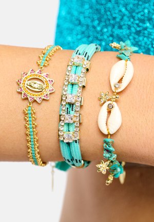 Ensemble de quatre bracelets : chaîne en or avec accents colorés, cordon turquoise ajustable avec strass, design en coquillage blanc et breloques florales.