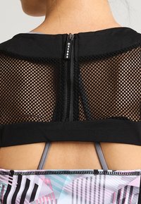 Top da donna in rete nera con zip centrale, colletto in tessuto nero e spalline colorate decorate visibili sotto.