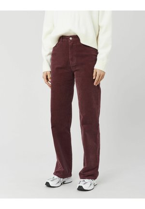 Pantalon en velours côtelé bordeaux à coupe droite, doté d'un design à cinq poches et d'une braguette à boutons. Porté avec un pull côtelé de couleur claire.