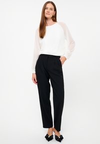 Witte blouse met doorzichtige mouwen, gecombineerd met hoge taille zwarte broek. Zwarte schoenen met grote strikken en parelaccenten. Eenvoudig ontwerp, getailleerde pasvorm.
