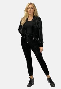 Czarny welurowy dres z zapinaną na zamek kurtką bombową i spodniami na sznurek, z wąskim krojem i teksturowanym materiałem. Uzupełniony czarnymi sneakersami.