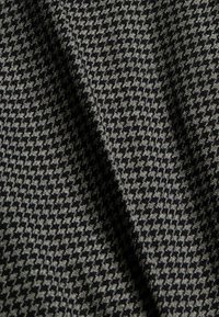 Tejido texturizado con un patrón de espiga en negro y gris, que presenta una superficie suave y un aspecto drapeado.