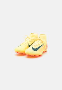 Scarpe da calcio gialle con upper testurizzato, logo Swoosh verde di Nike, accenti rosa sulla suola e design mid-top per supporto alla caviglia.