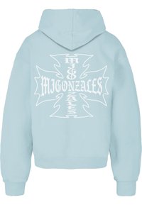 Svetlo modrá mikina s kapucňou s bielym grafickým dizajnom, ktorý obsahuje text "MIGONZALES" a dekoratívne akcenty na chrbte. Mäkká, štruktúrovaná tkanina.