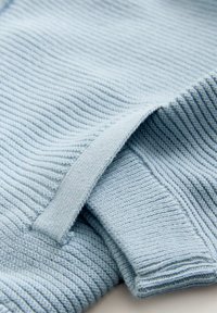 Vaaleansininen neulepaita, jossa on ribbineulostekstuuri. Siinä on käännetty hihansuu ja silmukkamallinen etikettikiinnitys, joka korostaa sen neulottua muotoilua.