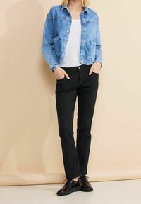 Jeansjacka i ljusblått med två framfickor, vit skjorta under, svarta byxor och svarta skor med snören. Enkelt mönster.