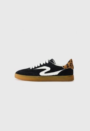 Sorte ruskind sneakers med hvid zigzag-stribe, hvide snørebånd, gummisål og pangfarvet leopardmønster på hælen, vist i sideprofil mod hvid baggrund.