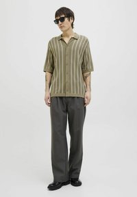 Strikket polo-shirt med korte ærmer i olivengrøn med lodrette lyse striber, parret med løse, mørkegrå bukser og sorte sko.