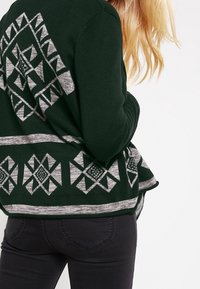 Mörkgrön cardigan med geometriska grå mönster på ryggen och i fållen. Mjuk textur med långa ärmar och en öppen frontdesign.