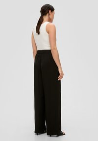 Zwarte wijde broek met een elastische tailleband, zachte textuur en een ontwerp tot op de grond, gecombineerd met een aansluitend wit mouwloos topje.