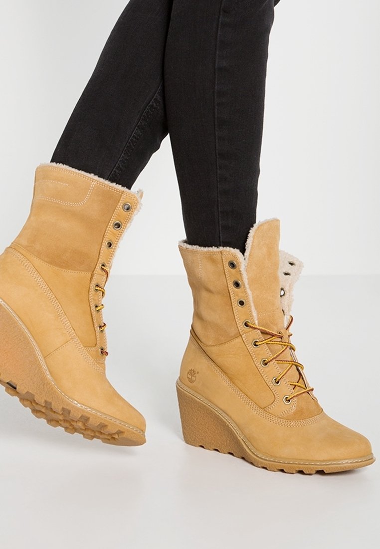 Bottes d'hiver beige à talon compensé avec doublure en fourrure et laçage à l'avant, portées avec un jean skinny noir sur un pied levé.