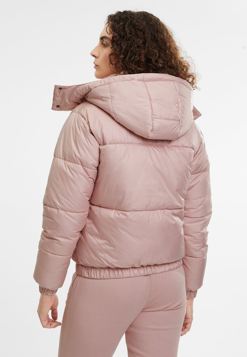 Giubbotto puffo rosa chiaro con cappuccio, caratterizzato da un design trapuntato e polsini e orlo elasticizzati. La vista posteriore mostra una leggera lucentezza e dettagli di cucitura.