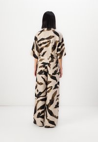 Ensemble en deux pièces composé d'un haut court à manches courtes, ample, et d'un pantalon à jambes larges, confectionné dans un tissu texturé au motif abstrait beige et noir.