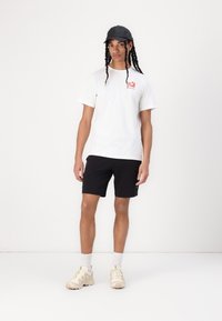 White cotton t-shirt with red logo, black shorts, and light beige sneakers. Accessories include a black cap. Simple and casual design.