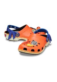 Oranje klompen met blauwe accenten, voorzien van uitsparingen en decoratieve charms. Gemaakt van lichtgewicht materiaal met een gestructureerde oppervlakte.