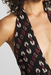 Top s halter krkem v černé látce se barevným květinovým a zvířecím potiskem, s hlubokým V výstřihem a jemnou texturou.