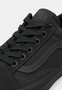 Svart Vans-sneaker med svarte lisser, ton-i-ton søm og signatur side stripe, nærbilde av overdelen og snøringene.