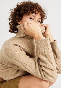 Pullover a collo alto di colore marrone chiaro, lavorato a maglia, con colletto e polsini a coste. Texture morbida con vestibilità rilassata e maniche lunghe.