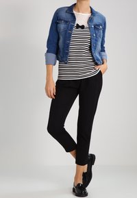 Jeansjakku, raidallinen musta-valkoinen toppi pitsikoristeilla, mustat lyhyet housut ja kiiltävät mustat loaferit. Yksinkertaiset muotoiluelementit näkyvissä.