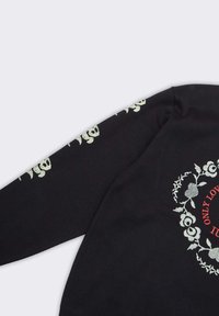 Maglione nero con motivo floreale argento e dettagli a forma di teschio sulle maniche. La parte anteriore mostra un testo rosso all'interno di un bordo ornato.