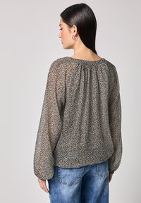 Gennemsigtig, sort og beige dyreprint-bluse med lange, voluminøse ærmer og rynket udskæring; båret over denimbukser.