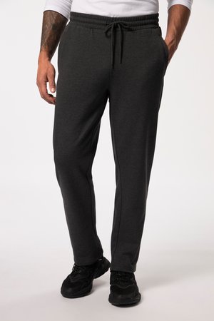 Mand iført mørkegrå sweatpants med snor og sorte sneakers, stående med hænderne i lommerne mod en ensfarvet lys baggrund.