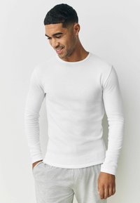 White, long-sleeve ribbed t-shirt with a round neckline, fitted design, and smooth texture, paired with gray sweatpants.