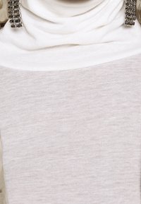 Hvid, tætsiddende top med draperet halsudskæring og tekstureret stof. Har et lagdelt udseende med en glat, let fremtoning.