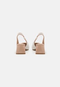 Scarpe slingback bianche con texture, con tacco in vernice beige, che presentano un dettaglio a fibbia e una finitura solida e liscia sul tacco.