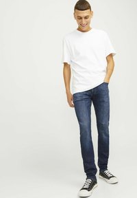 Camiseta de algodón blanca, jeans de mezclilla azul oscuro con corte ajustado y zapatillas negras con suelas blancas. Sin patrones o acentos notables.