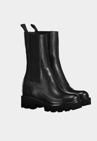 Zwarte leren enkellaarsjes met een gladde textuur, elastische zijkanten en dikke rubberen zolen met een grof profiel.